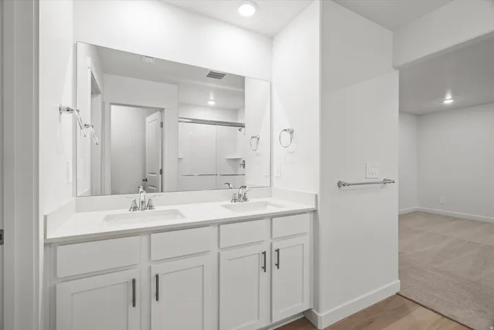 Dual vanity with white cabinetry, integrated sinks, chrome fixtures, and a large wall-mounted mirror