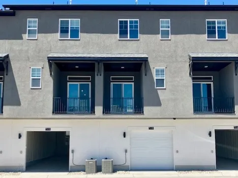 Contemporary multi-level townhome exterior featuring a stucco facade, multiple private balconies with black railings, and attached garages