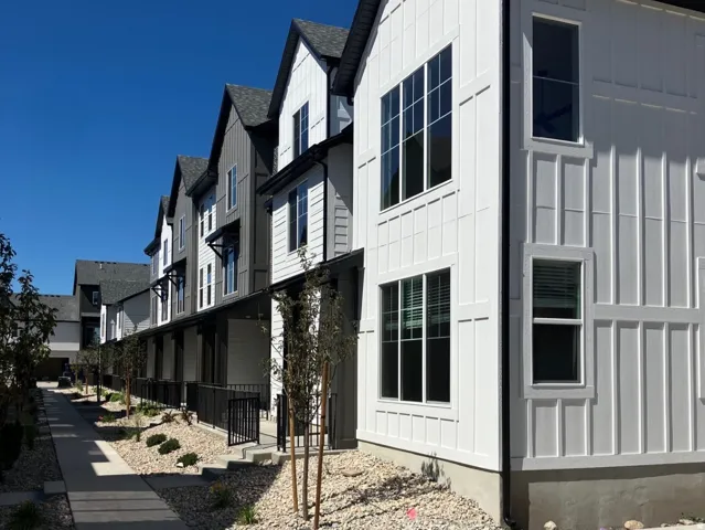 Contemporary multi-level townhome featuring a board and batten facade, dark-framed windows, and a covered entry with a black railing