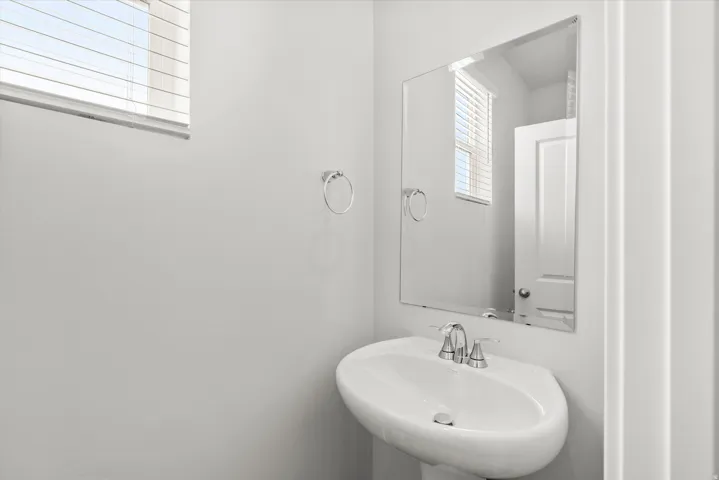 Bright bathroom featuring a curved pedestal sink with chrome faucet, large framed mirror with integrated lighting, and clean white finishes throughout
