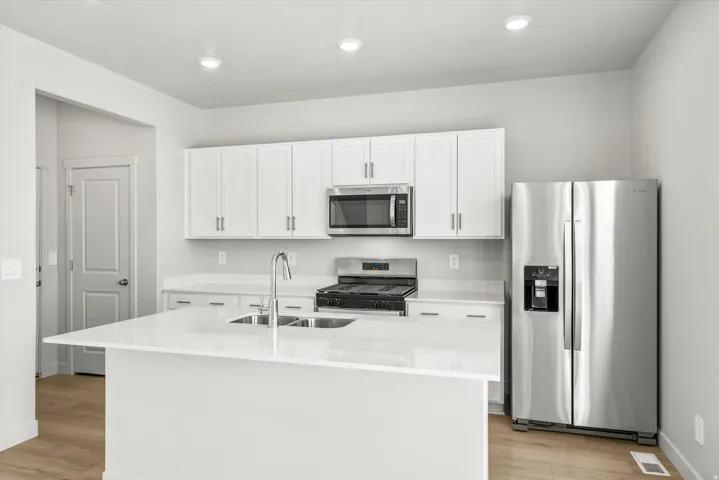 Modern kitchen featuring white cabinetry with chrome hardware, a large waterfall-edge island with white quartz countertop, stainless steel appliances including a gas cooktop and built-in microwave, and recessed ceiling lighting
