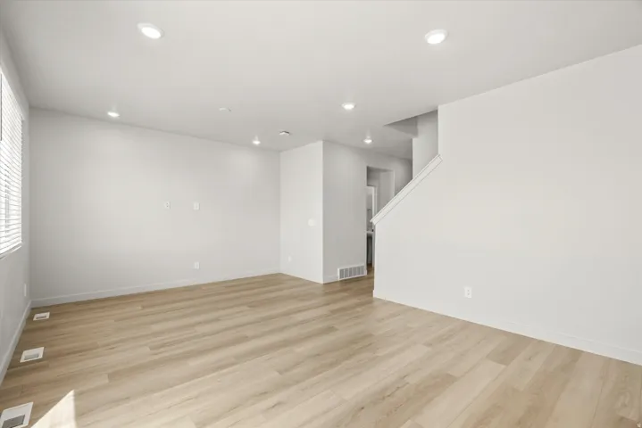 Spacious open room featuring warm wood-finish flooring throughout, recessed ceiling lighting, and clean white walls with multiple electrical outlets