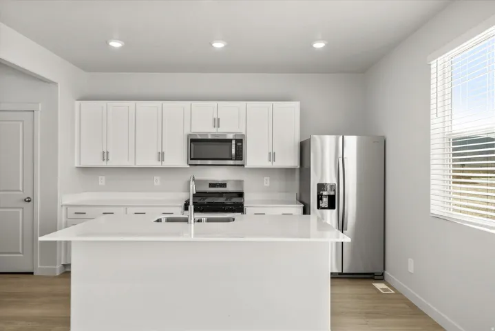 Modern kitchen featuring white shaker-style cabinetry, stainless steel appliances including a built-in microwave and refrigerator with ice/water dispenser, quartz countertops, and a large waterfall-edge island
