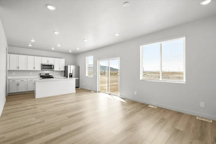 Open-concept living space with wood-finish flooring, white cabinetry, integrated kitchen island, stainless steel appliances, and abundant natural light from large windows and sliding glass door