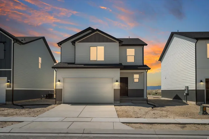 **DISCLAIMER** Elevation may vary. Modern two-story residence featuring a clean-lined facade with light gray siding, a two-car garage with paneled door, and illuminated exterior sconce lighting