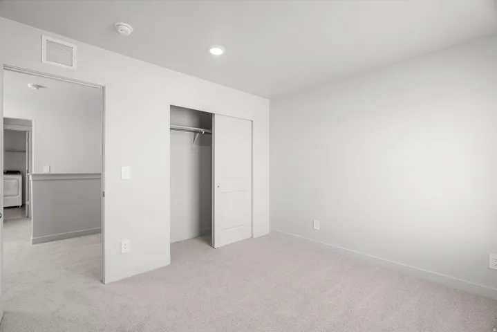 Spacious bedroom with neutral carpeting, multiple closets including a reach-in closet with shelving and rod, recessed ceiling lighting, and white walls with electrical outlets