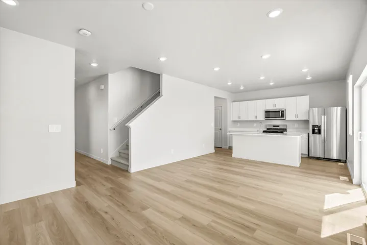 Open-concept living area featuring gleaming wood-finish flooring throughout, recessed ceiling lighting, and a modern kitchen with white cabinetry, stainless steel appliances, and a center island