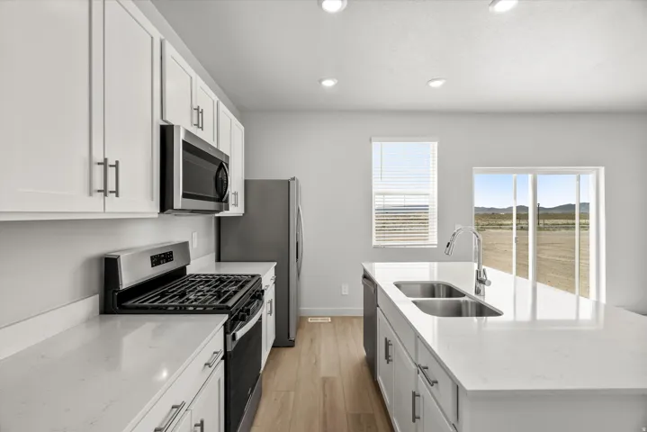 Contemporary kitchen featuring white cabinetry, stainless steel appliances, light-toned wood-finish flooring, a kitchen island with a double basin sink, and a sliding glass door