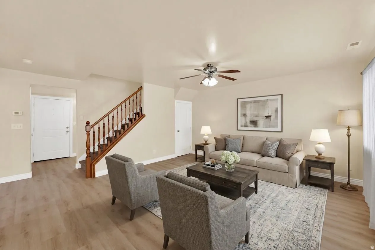 Inviting living area featuring wood-finish flooring, a traditional wood staircase, and a ceiling fan with light fixture