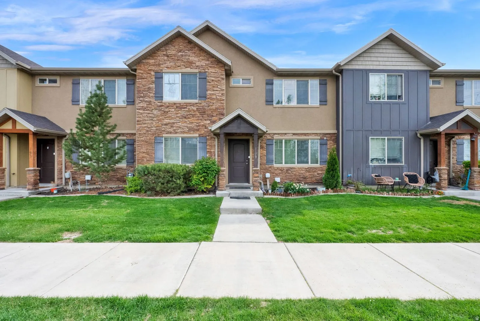 Stone and stucco exterior with dark shutters, featuring a covered entry and a front lawn with established landscaping