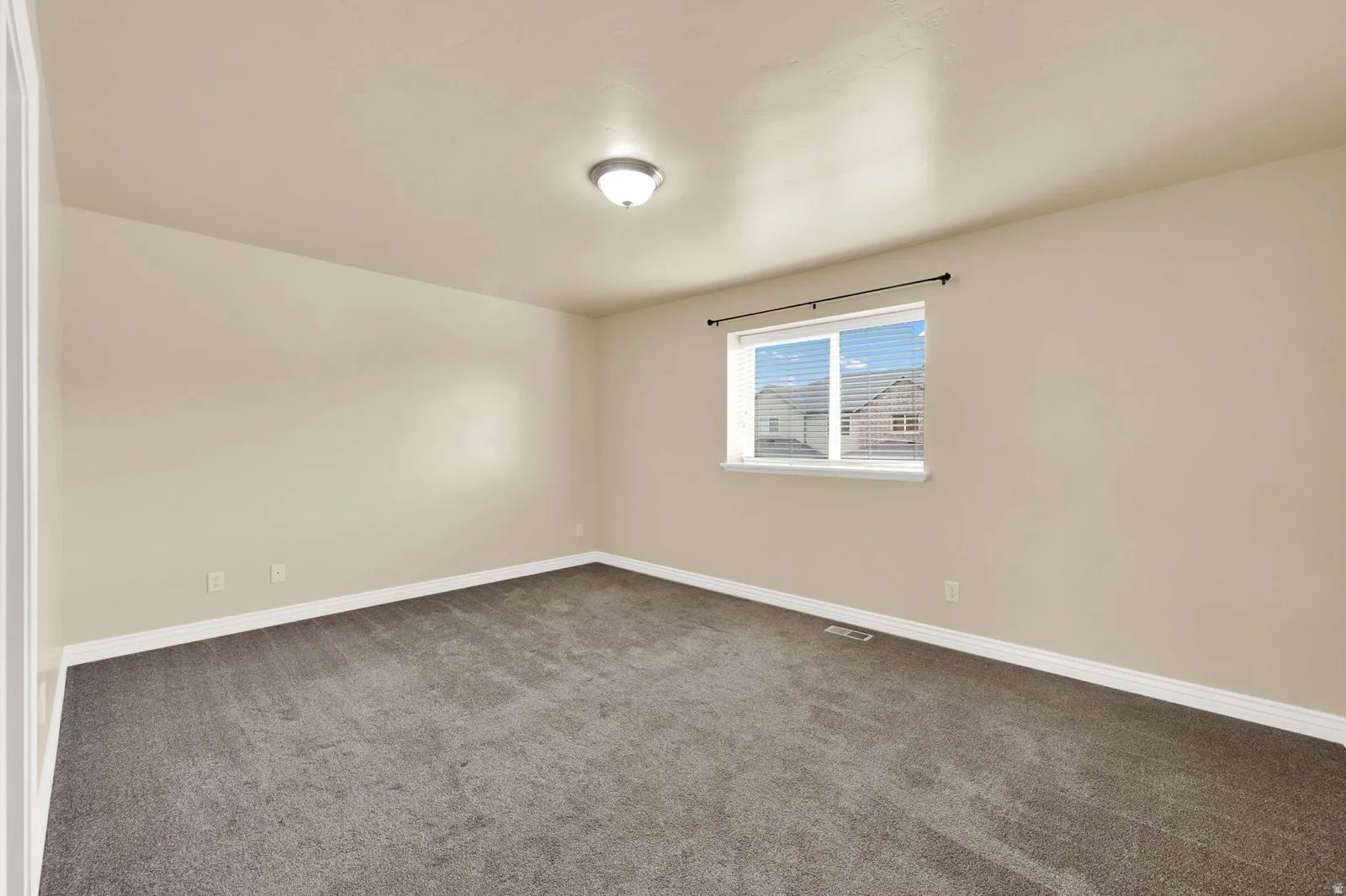 Interior room featuring neutral wall paint, dark grey carpet, white baseboards, and a single window with blinds