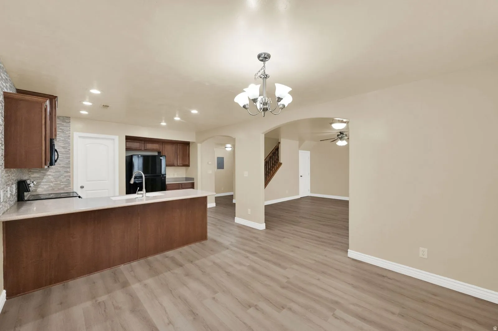 Open-concept living space featuring wood-finish flooring, a kitchen island with integrated sink, dark wood cabinetry, and a textured tile backsplash