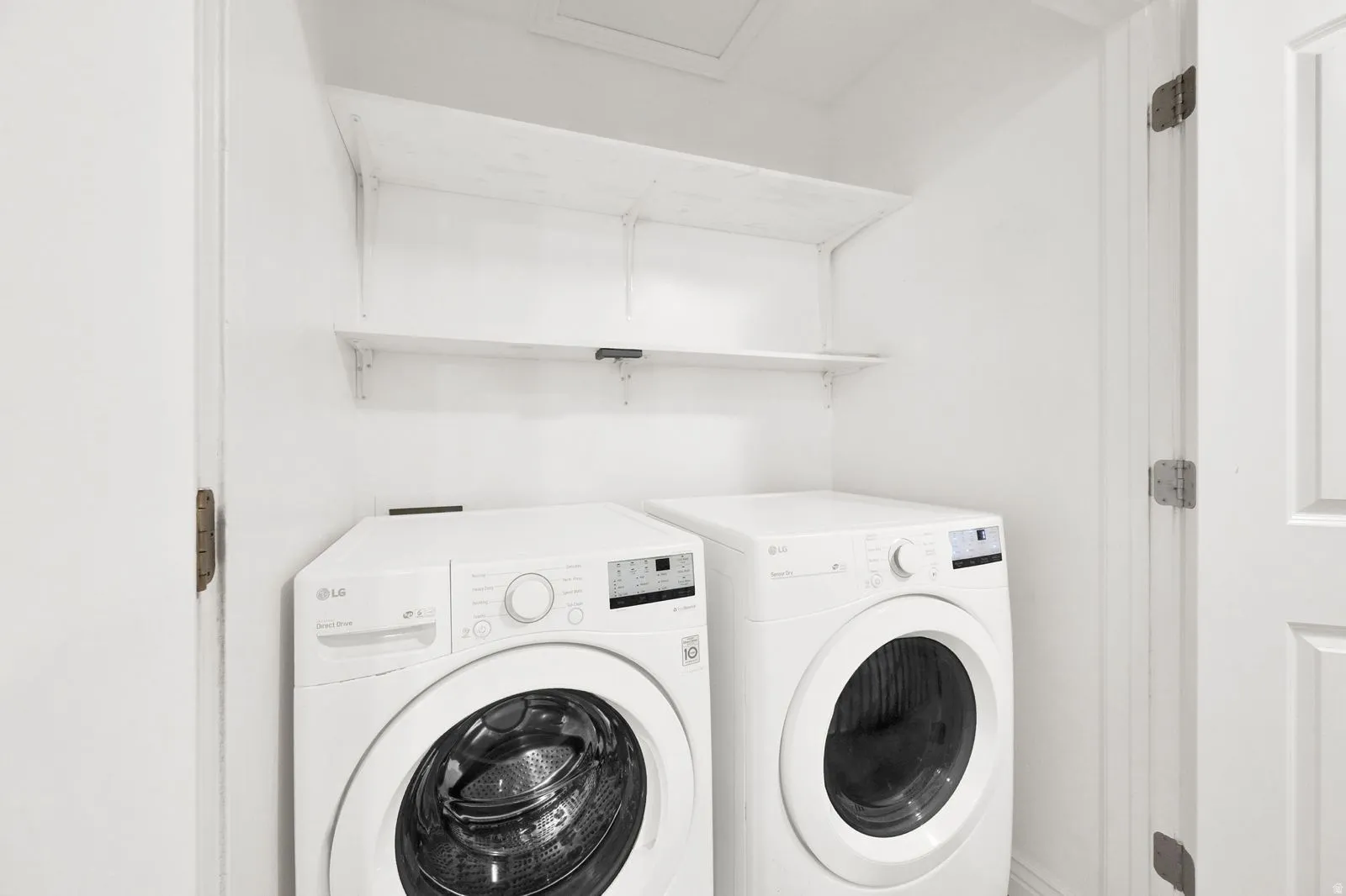 Dedicated laundry area featuring a white front-load washer and dryer set, white shelving, and white walls