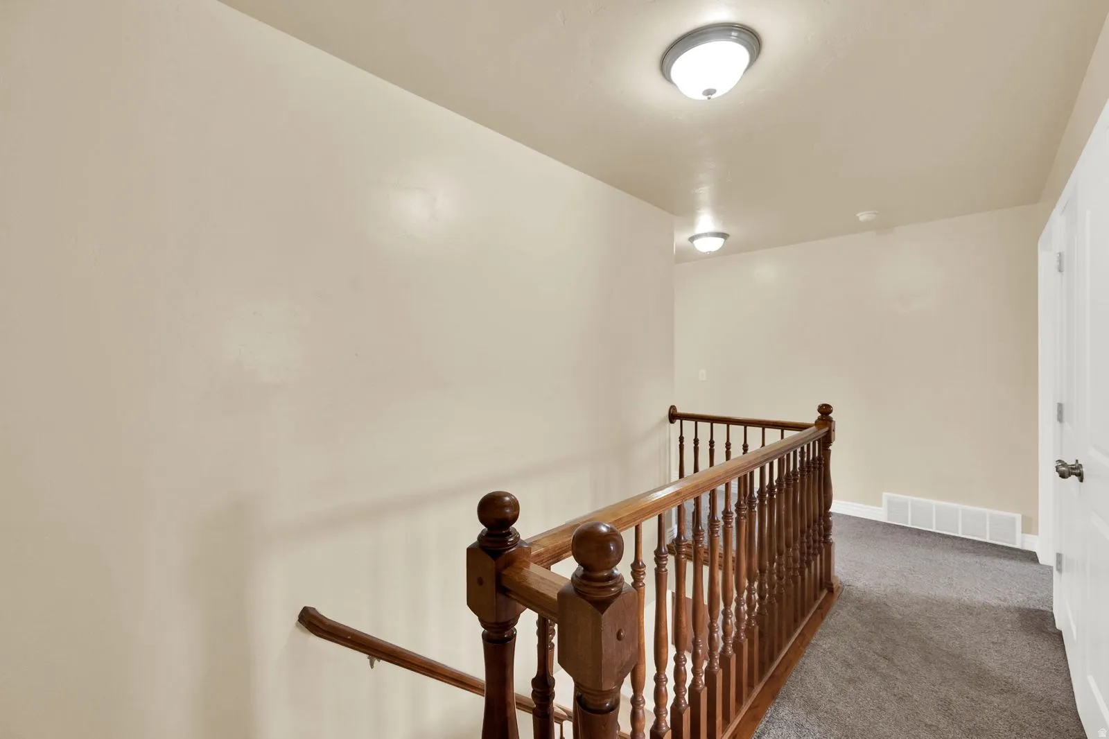 Upper-level landing featuring a wood banister, neutral-toned walls, and flush-mount lighting