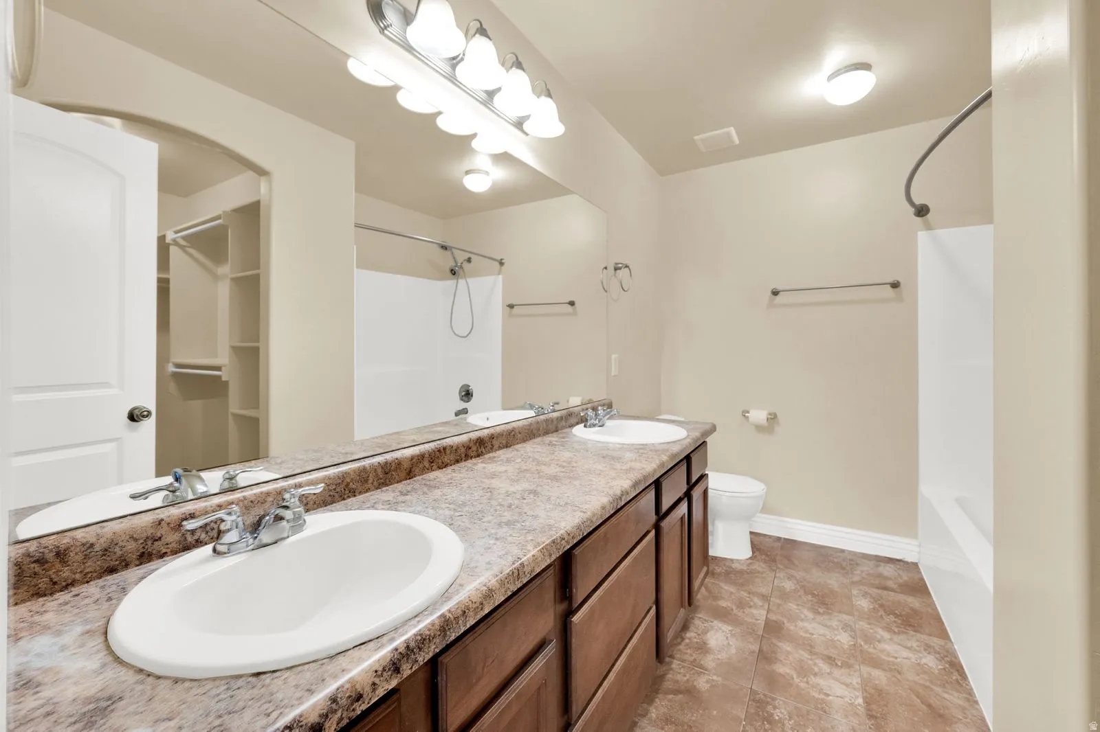 Bathroom featuring a double vanity with integrated oval sinks and chrome fixtures, wood-finish cabinetry, a large mirror, and overhead vanity lighting