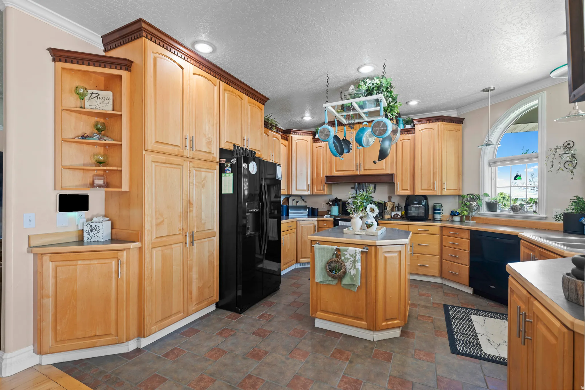 Kitchen featuring abundant light wood-finish cabinetry, a central island with countertop, and black appliances