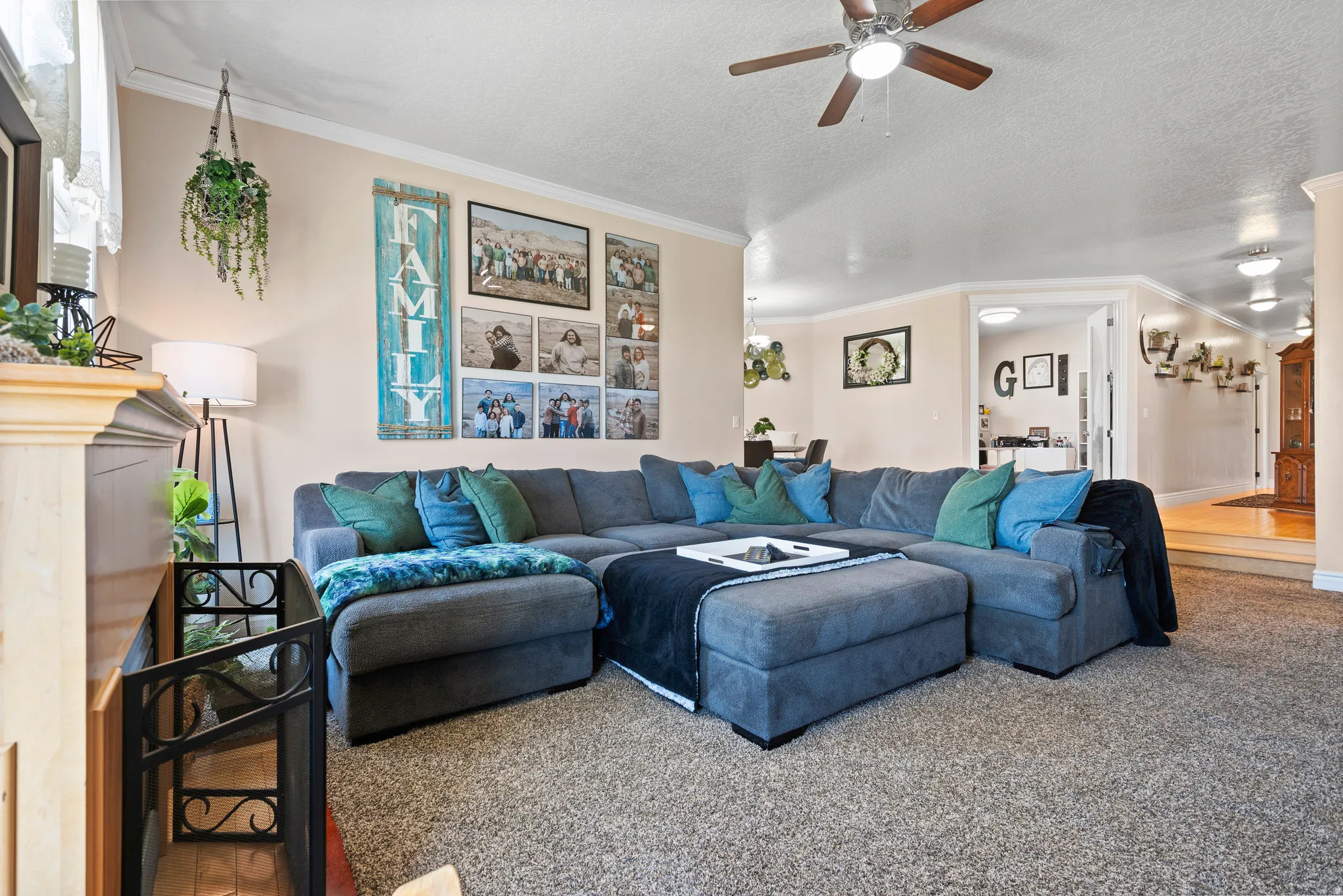 Carpeted living area featuring a ceiling fan with integrated lighting, crown molding, and neutral wall tones