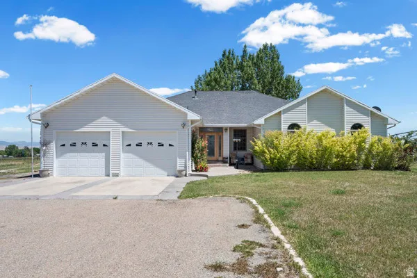 Ranch-style residence featuring a two-car garage, mature landscaping, and a partial gravel driveway
