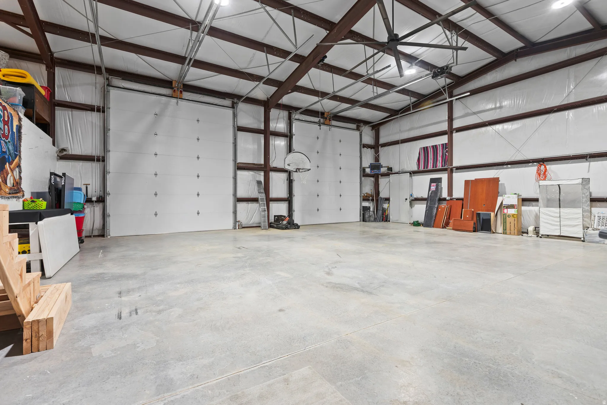 Spacious industrial interior featuring a large concrete floor, exposed metal beam ceiling, multiple roll-up doors, and overhead lighting