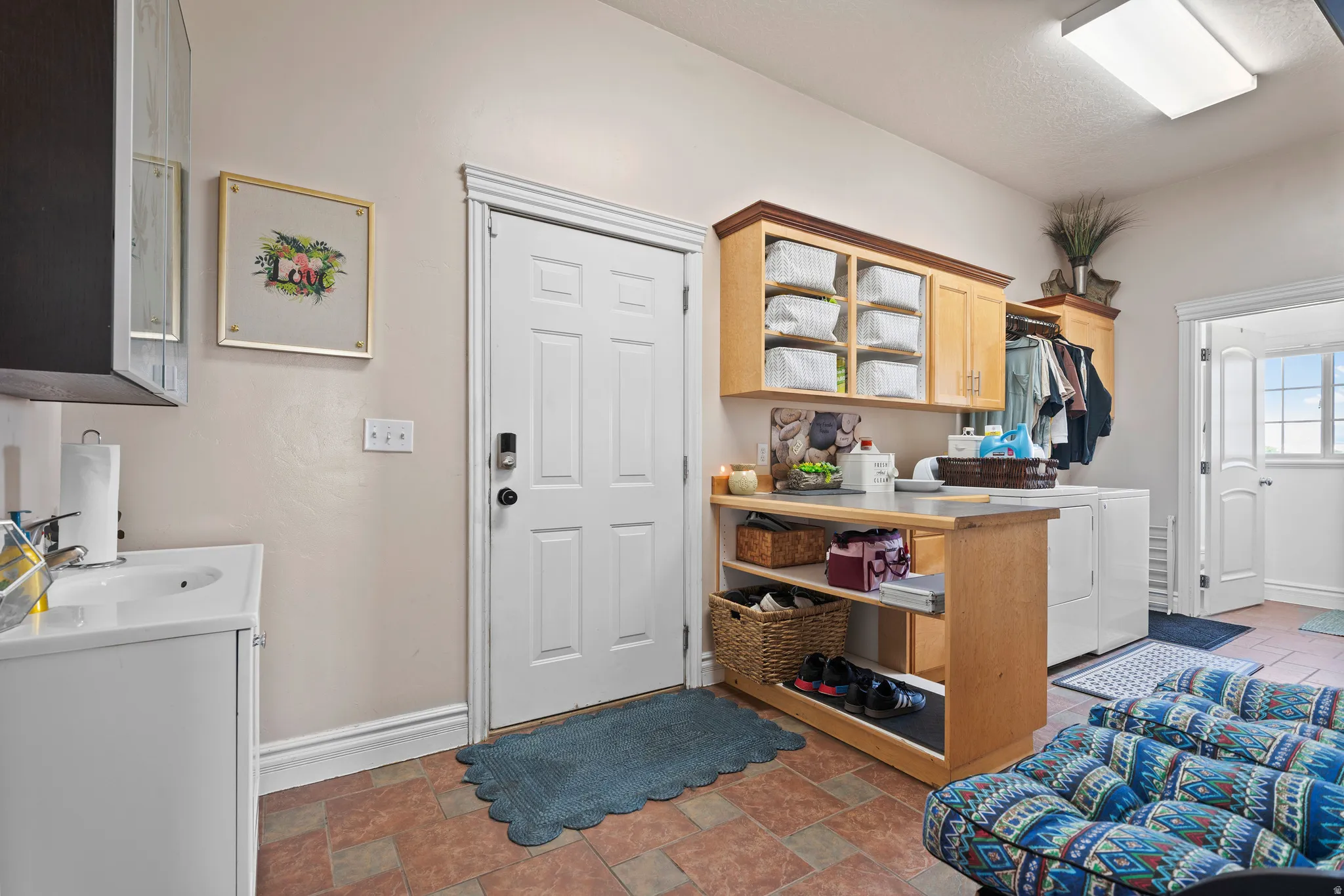Utility room featuring a white paneled door, light wood cabinetry, a utility sink with a white vanity, and terra cotta-style floor tiles