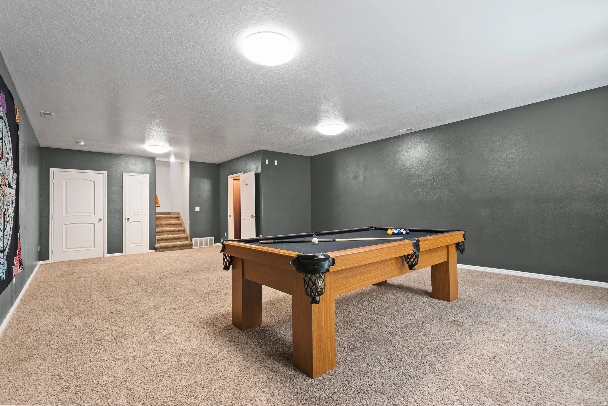 Spacious recreational room featuring carpet flooring, dark gray walls, and multiple flush-mount ceiling lights