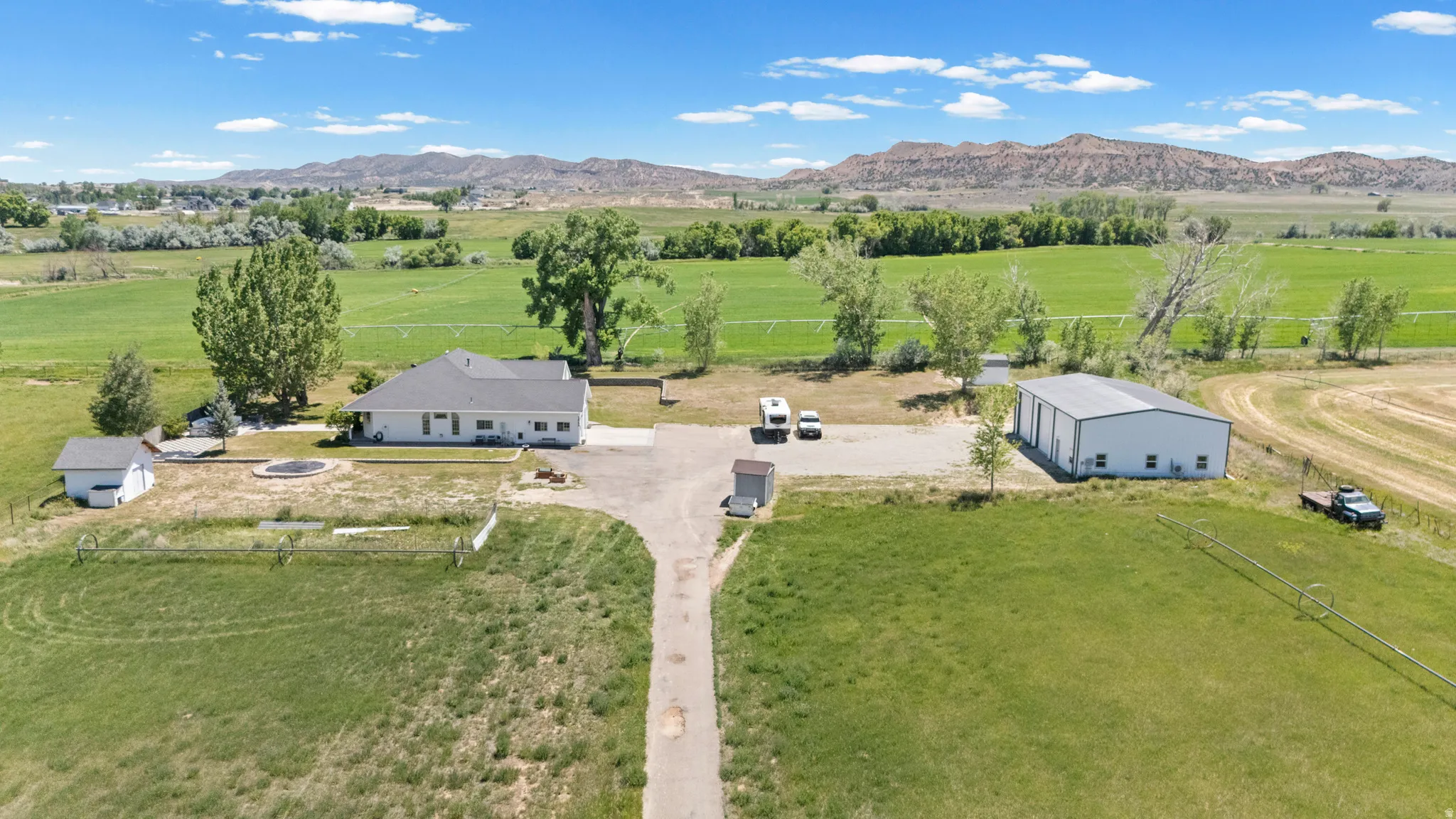 Expansive property featuring a single-story residence, separate workshop building, detached shed, paved driveway, and open fields