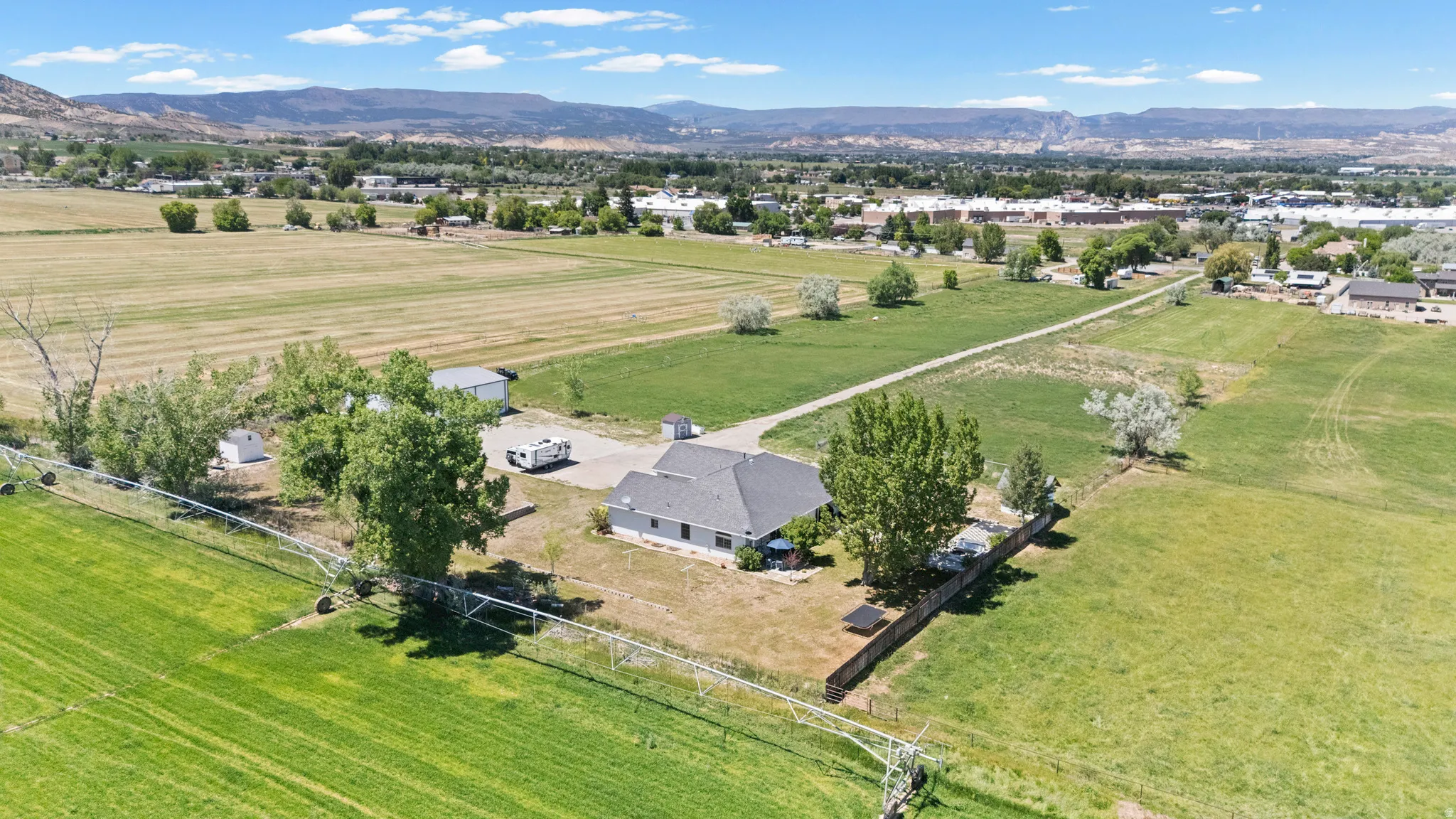 Expansive property featuring a single-story residence with a dark shingle roof, surrounded by mature trees and verdant acreage