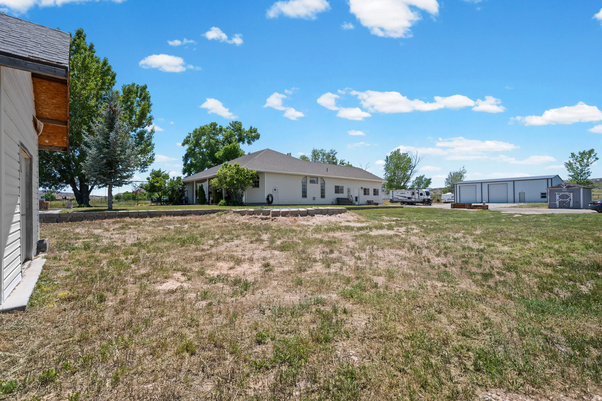 Spacious property with a large, undeveloped yard, featuring a single-story residence with a light-colored exterior and a dark roof