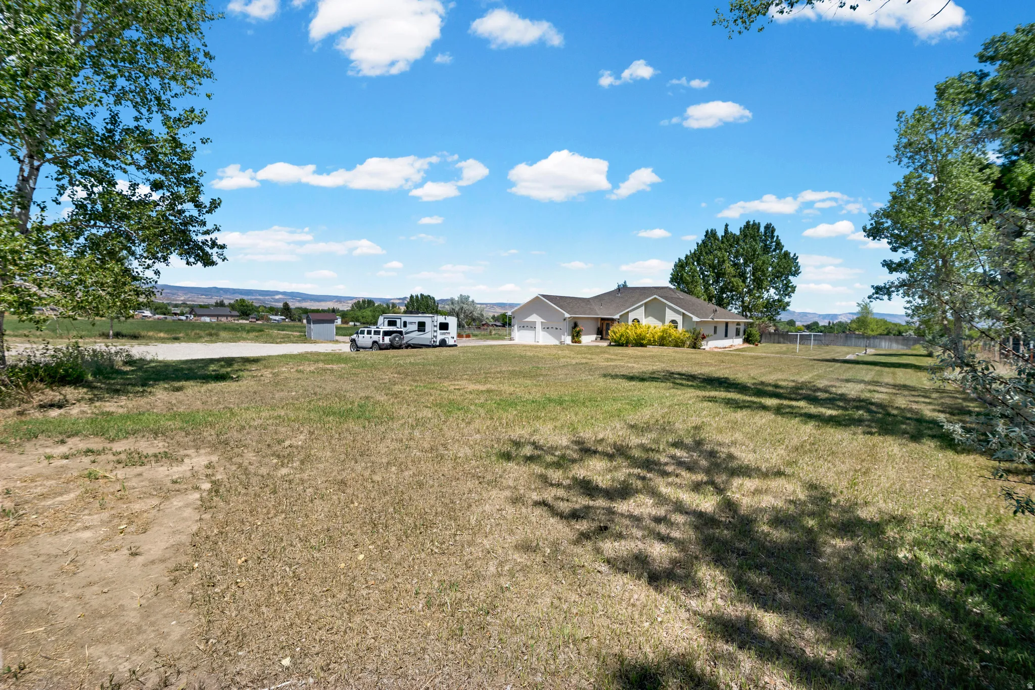 Expansive property featuring a ranch-style home with an attached two-car garage, surrounded by a large grassy area and mature trees