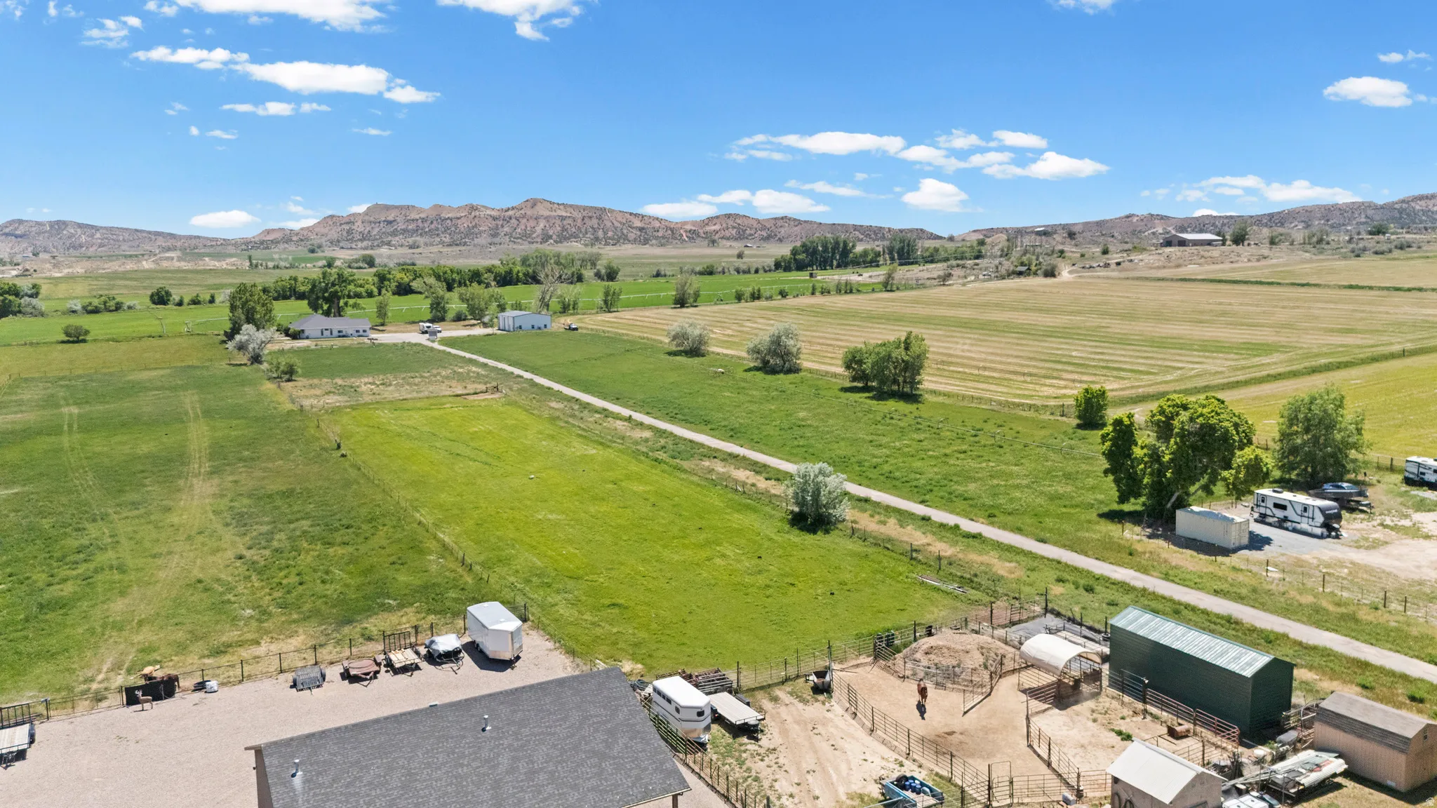 Expansive rural property featuring a gravel driveway, fenced enclosures, a large metal outbuilding, and distant mountain backdrops