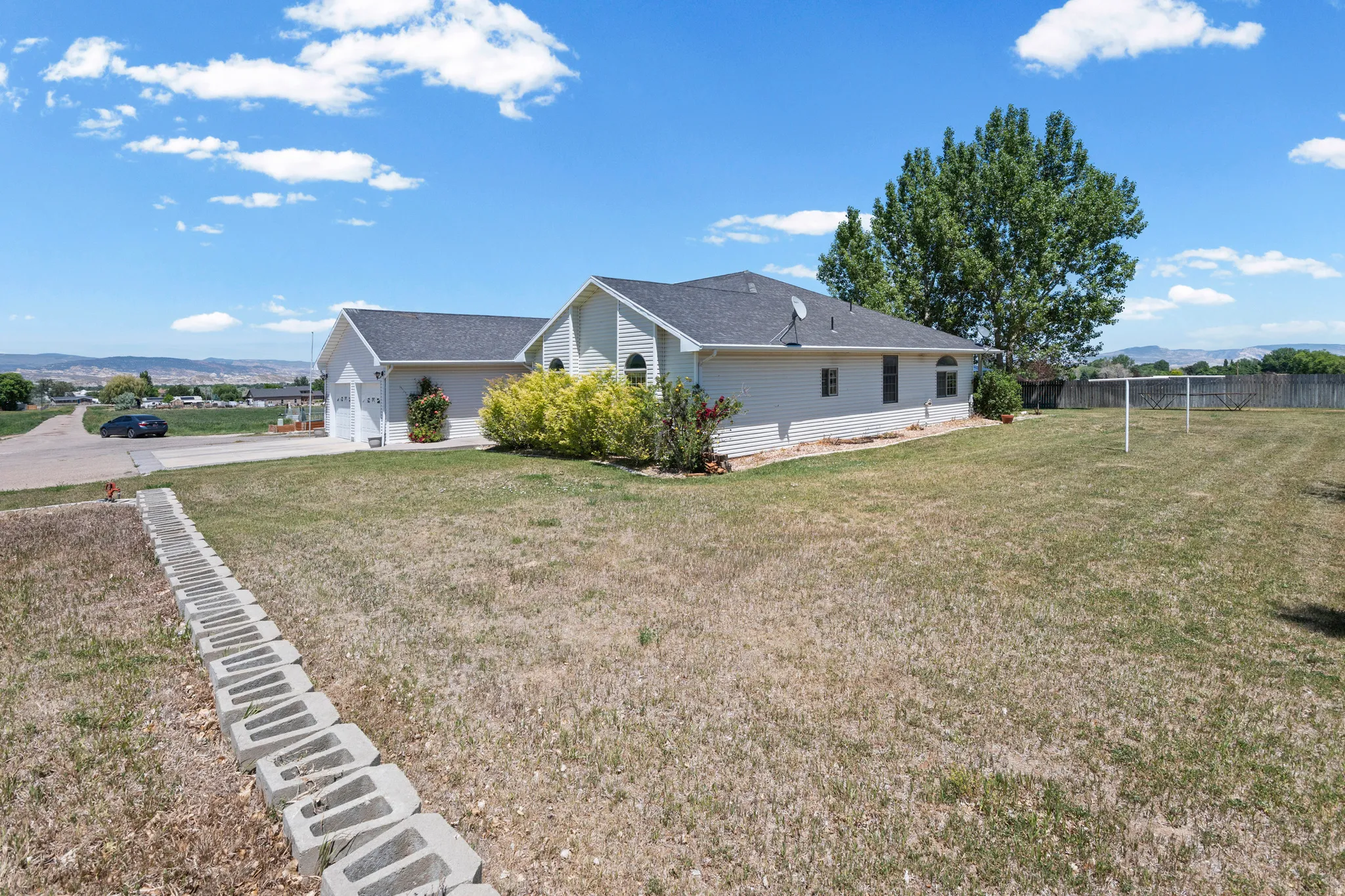 Ranch-style residence featuring a prominent front lawn, a two-car attached garage, and a gravel driveway