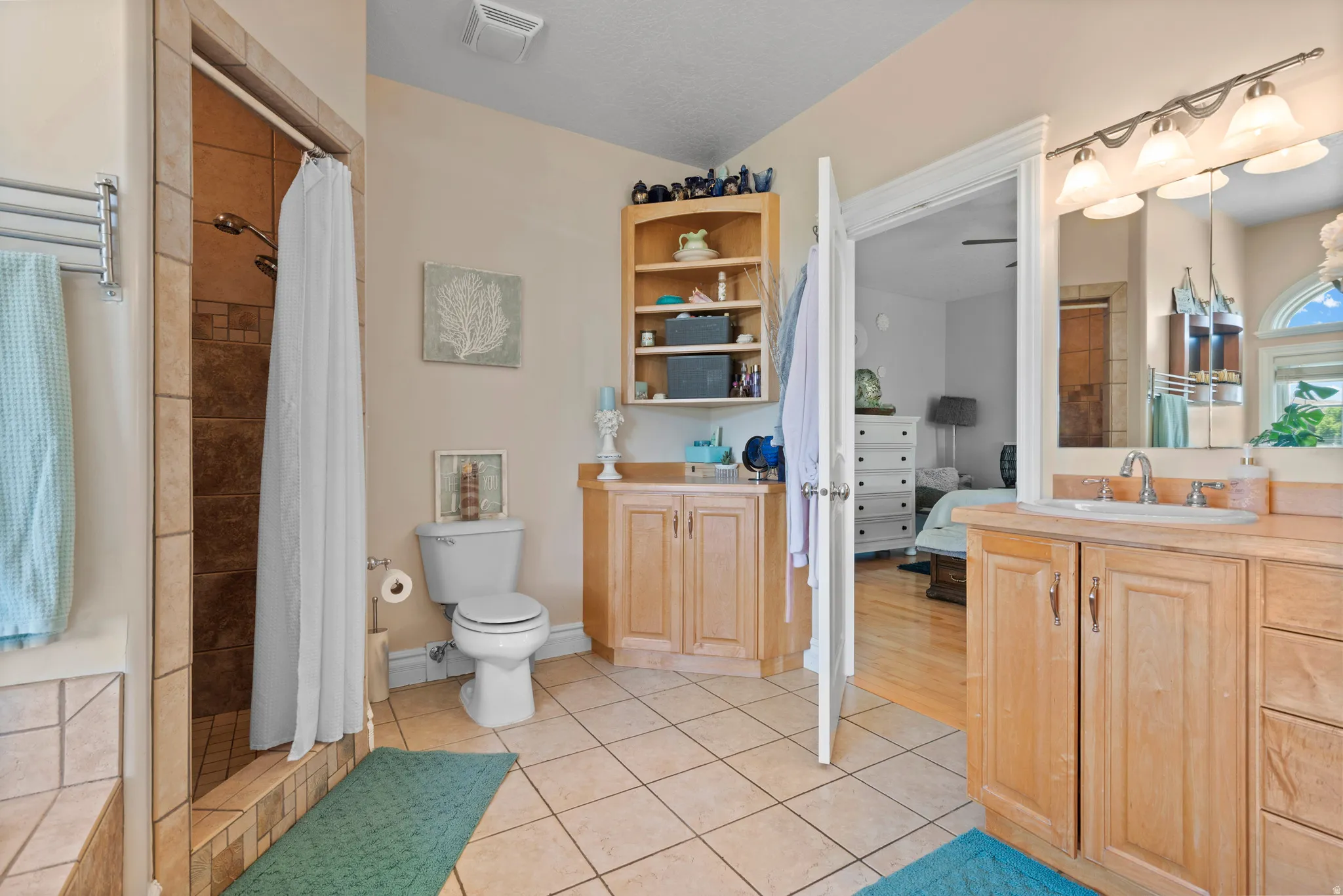 Bathroom featuring a tiled floor, walk-in shower with tiled surround, wood-finish vanity with an integrated sink, mirror, and sconce lighting