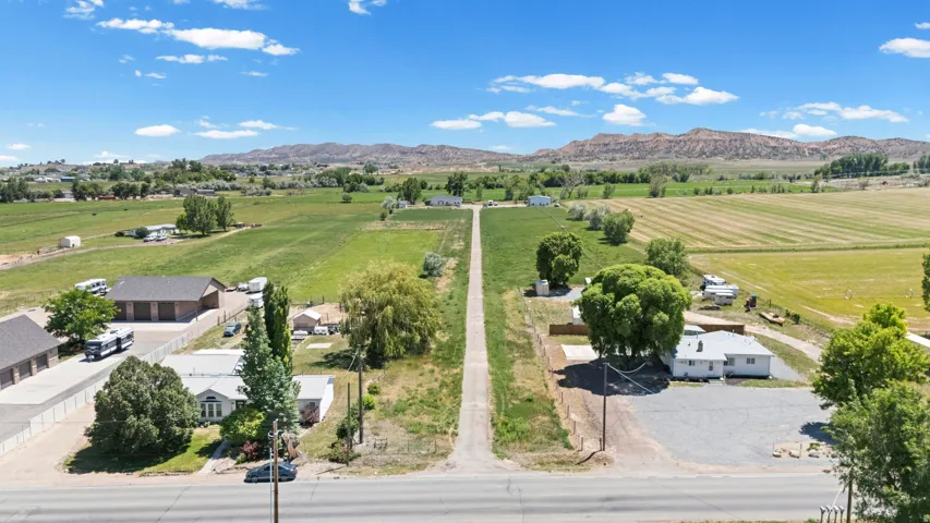 Expansive rural property featuring an elongated driveway, multiple structures, and a backdrop of verdant fields and distant mountains