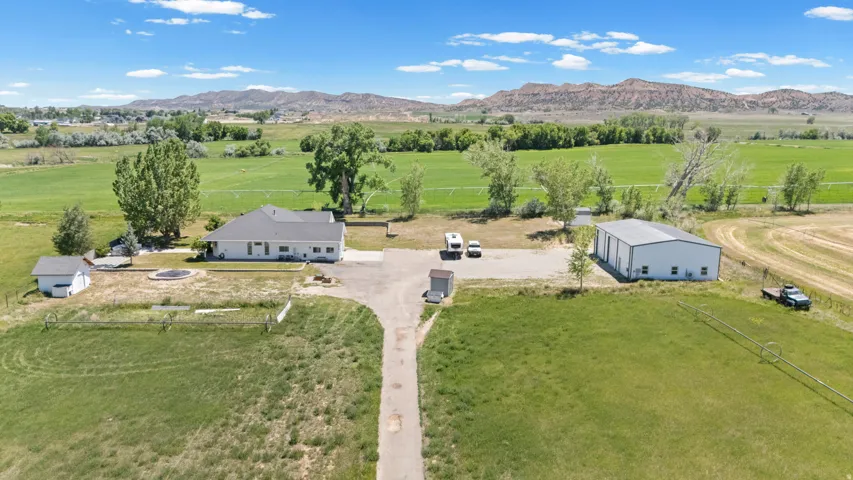 Expansive property featuring a single-story residence, separate workshop building, detached shed, paved driveway, and open fields