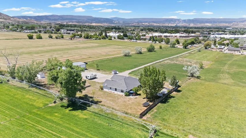 Expansive property featuring a single-story residence with a dark shingle roof, surrounded by mature trees and verdant acreage