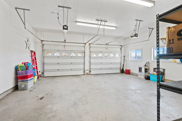 Two-car garage featuring automatic garage door openers, concrete flooring, and multiple windows