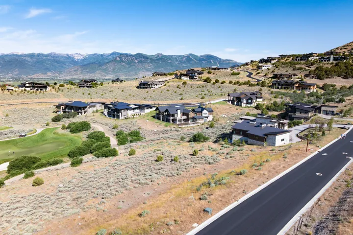 Expansive residential development featuring modern architecture, mountain backdrop, paved roadways, and proximity to a golf course
