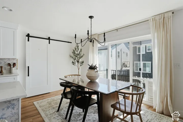 Dining area featuring wood-finish flooring, a contemporary chandelier, and a sliding glass door with balcony access