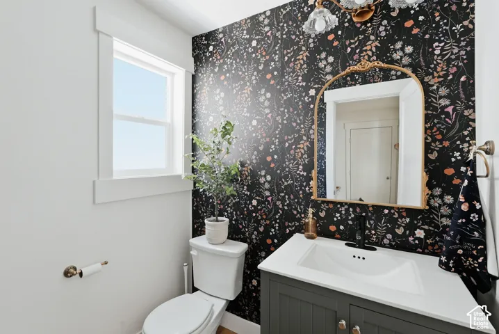 Powder room featuring a floral accent wall, a gold-framed arched mirror, a single vanity with a white countertop, and a built-in sink with a matte black faucet