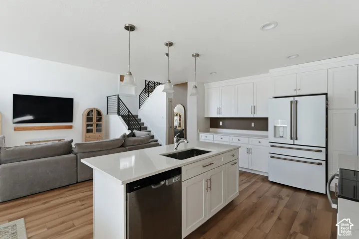 Open-concept living area featuring a white kitchen with shaker cabinetry, a center island with sink and dishwasher, and wood-finish flooring