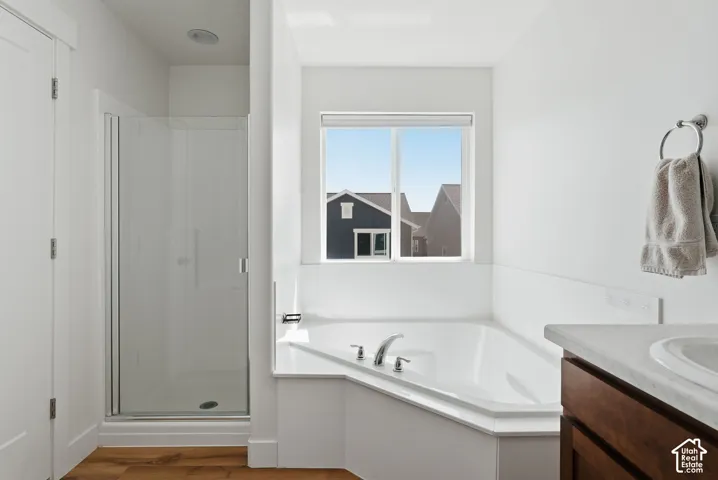 Bathroom featuring a corner soaking tub with chrome fixtures, a separate glass-enclosed shower, and wood-finish flooring