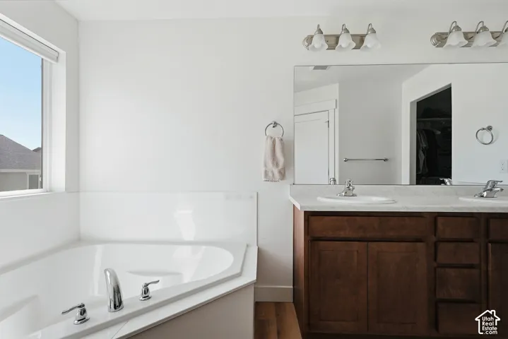 Spacious bathroom featuring a corner soaking tub with chrome fixtures, a dual-sink vanity with wood-finish cabinetry, a large wall-mounted mirror, and overhead vanity lighting