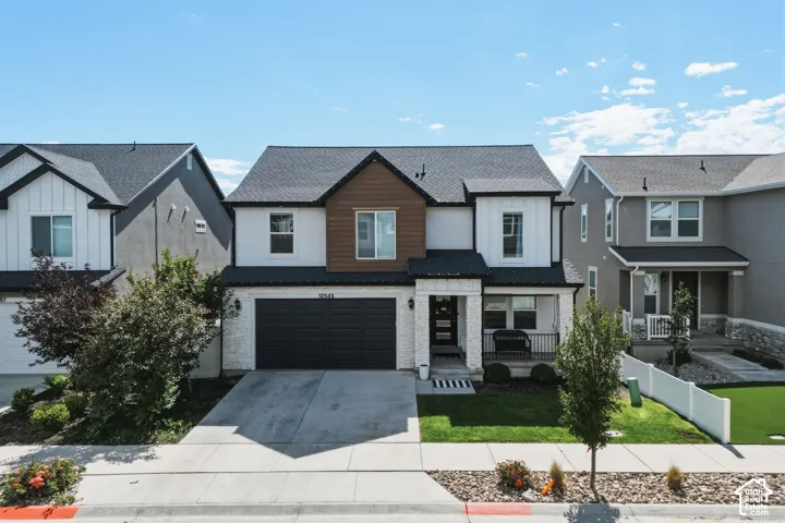 Contemporary two-story residence featuring a two-car garage, covered porch, dark shingle roof, and mixed material facade with white brick, vertical siding, and wood-finish siding accents