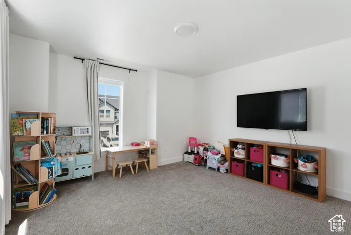Spacious room featuring neutral carpeting, white walls, and a single window with a black rod and light-toned drapes