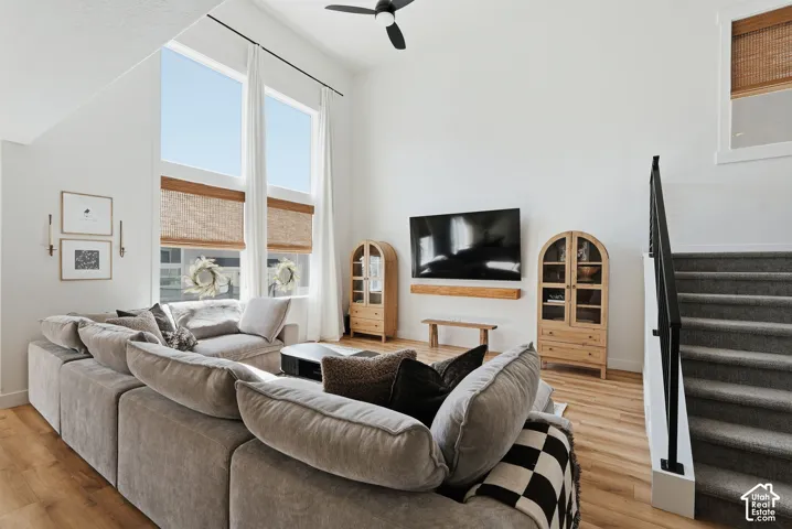 Vaulted living room featuring wood-finish flooring, a ceiling fan, and large windows with natural light