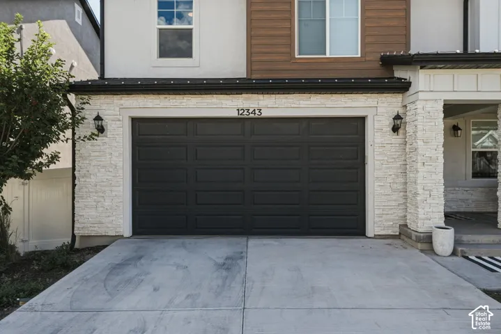 Modern exterior featuring a dark paneled garage door, stacked stone siding, and a concrete driveway