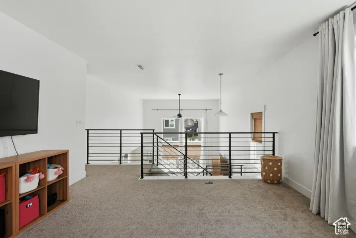 Carpeted loft area featuring a modern black metal horizontal railing, white walls, and recessed lighting