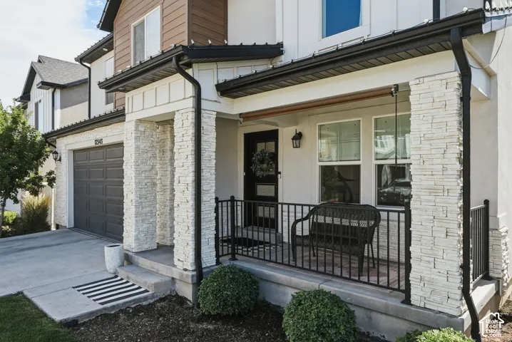 Contemporary home exterior featuring stacked stone columns, a covered porch with black railings, and a two-car garage with a panelized door