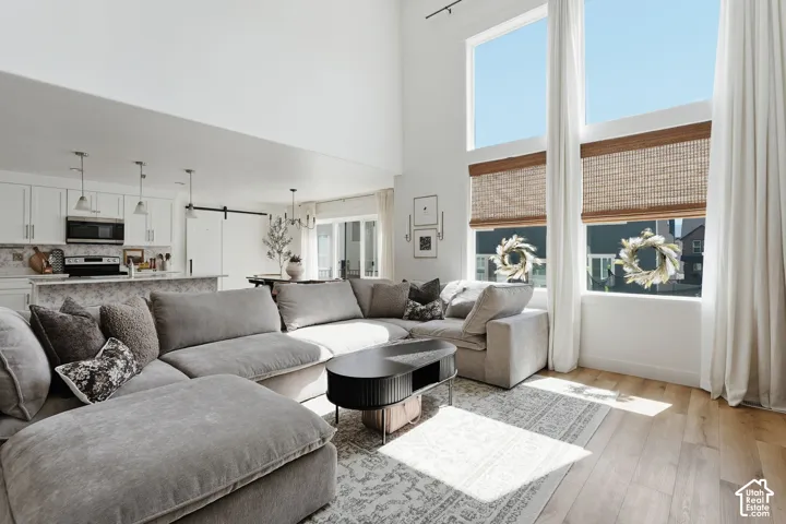 Two-story living area with high ceilings and expansive windows, wood-finish flooring, and an open-concept design that incorporates a kitchen with white cabinetry and a patterned backsplash