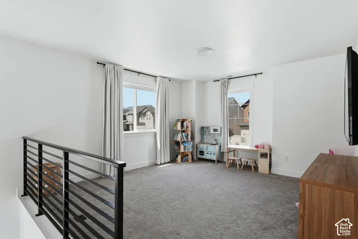 Spacious upper-level loft featuring two windows with drapery, a contemporary black metal railing, overhead lighting, and carpet flooring